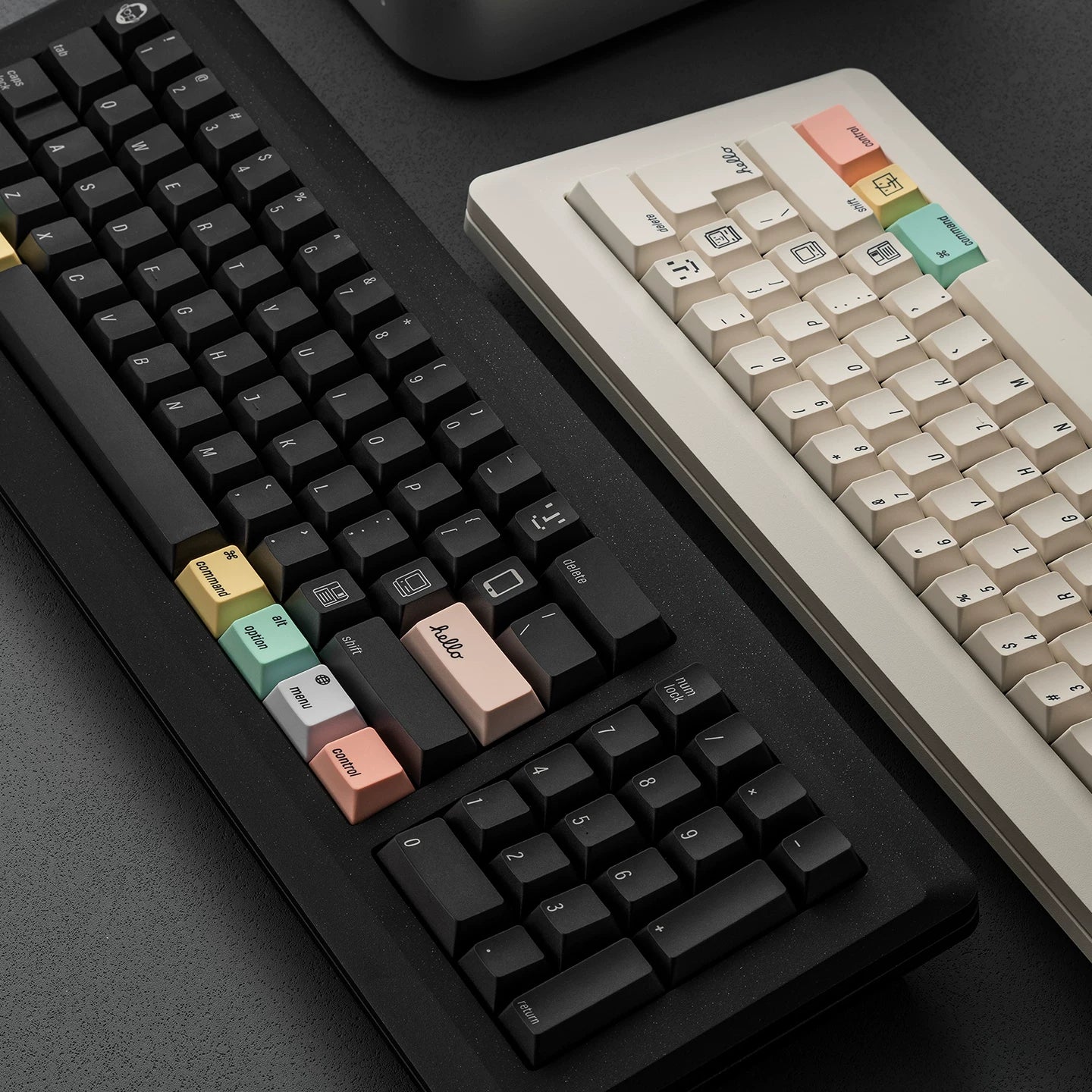 Two mechanical keyboards shown on a dark tabletop: a black keyboard in the foreground with pastel-colored keycaps, and a cream-colored keyboard partially visible behind it.