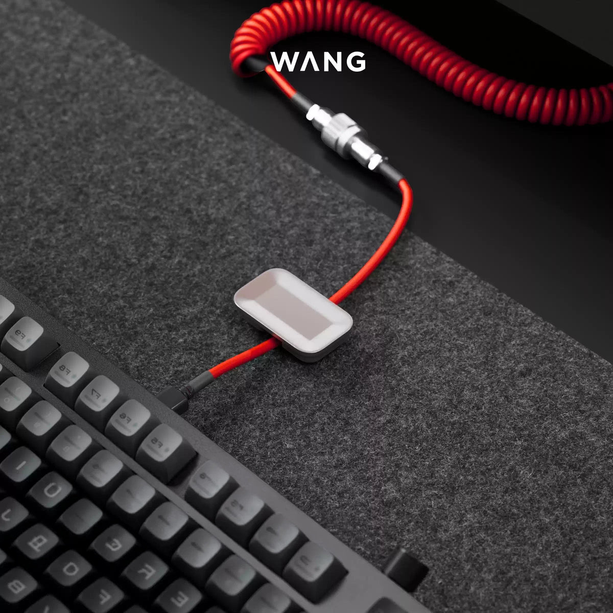 Gwang magnetic cable organizer in titanium-look zinc alloy holding a red coiled cable on a grey desk mat.