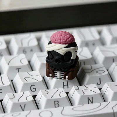 OZO Keyboards artisan keycap featuring a black skull with an exposed pink brain and white bandages on a white keyboard