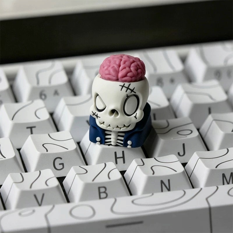 OZO Keyboards artisan keycap featuring a cartoon skull with an exposed pink brain and blue jacket on a white keyboard