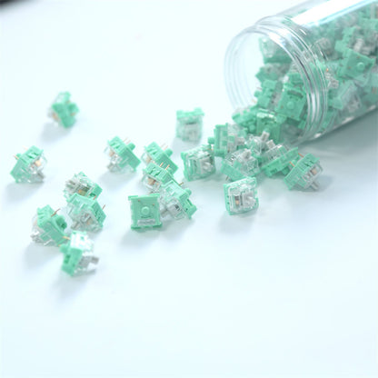 Mint green mechanical switches spilling out of a clear container on a white background