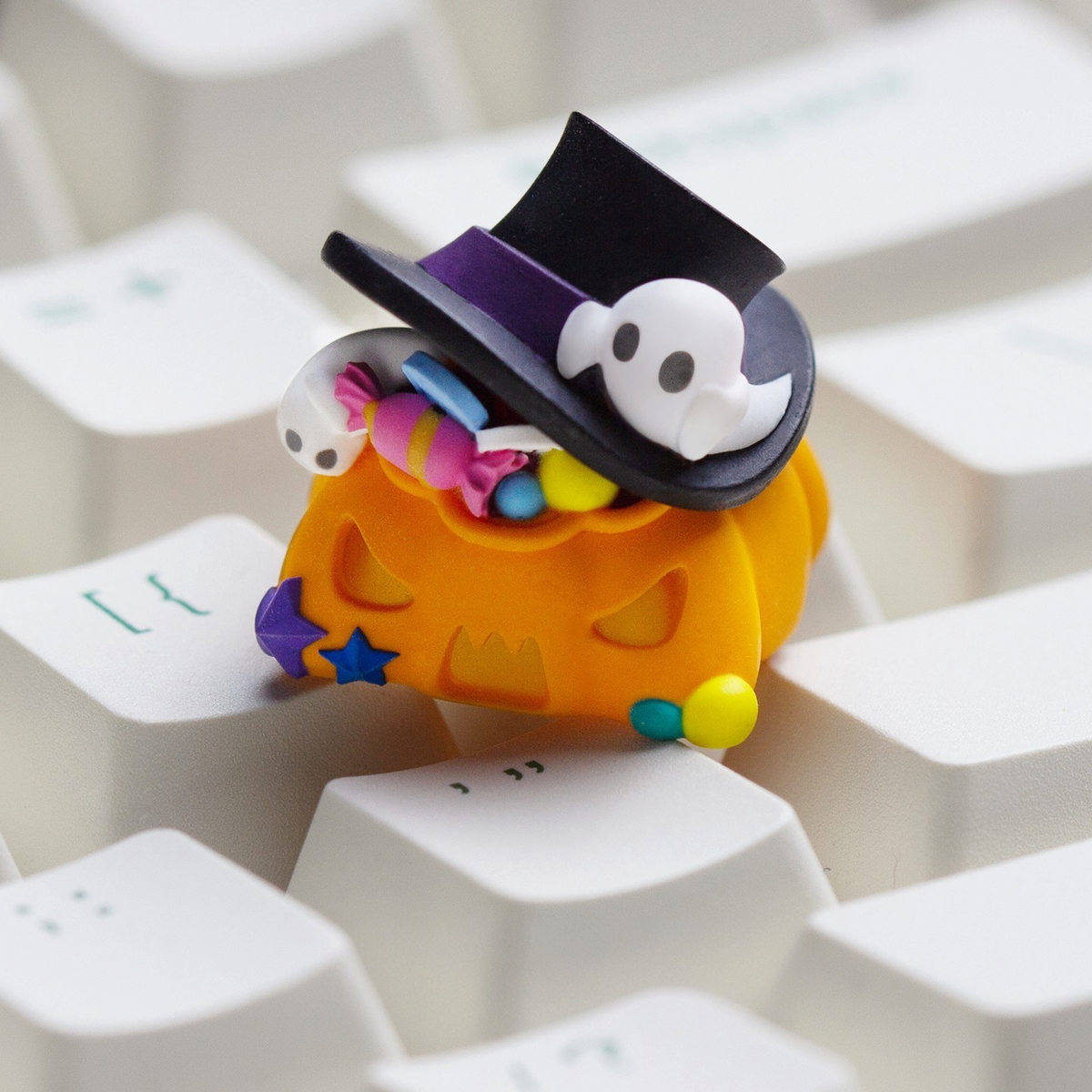 OZO Keyboards Halloween pumpkin artisan keycap featuring a black top hat, ghost, and colorful candy on a white keyboard