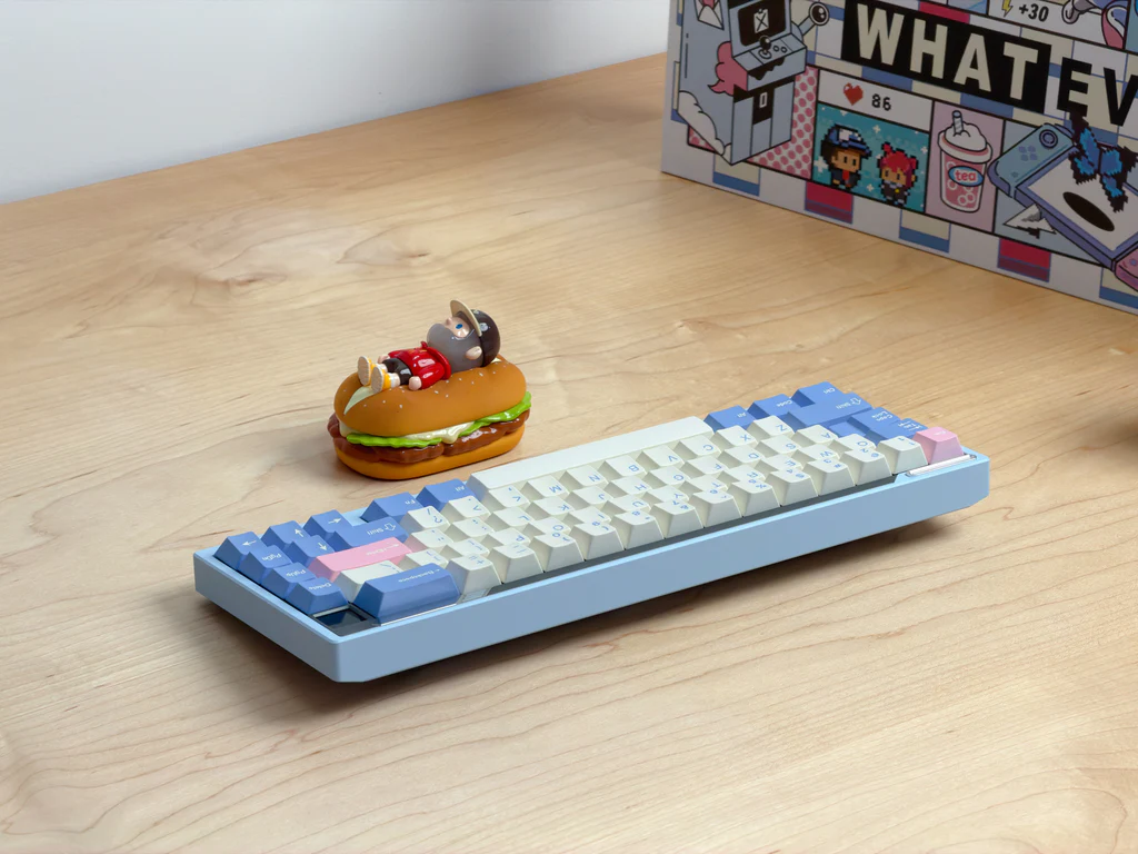 Small keyboard with unique keycaps on a wooden surface next to a hamburger-shaped object.