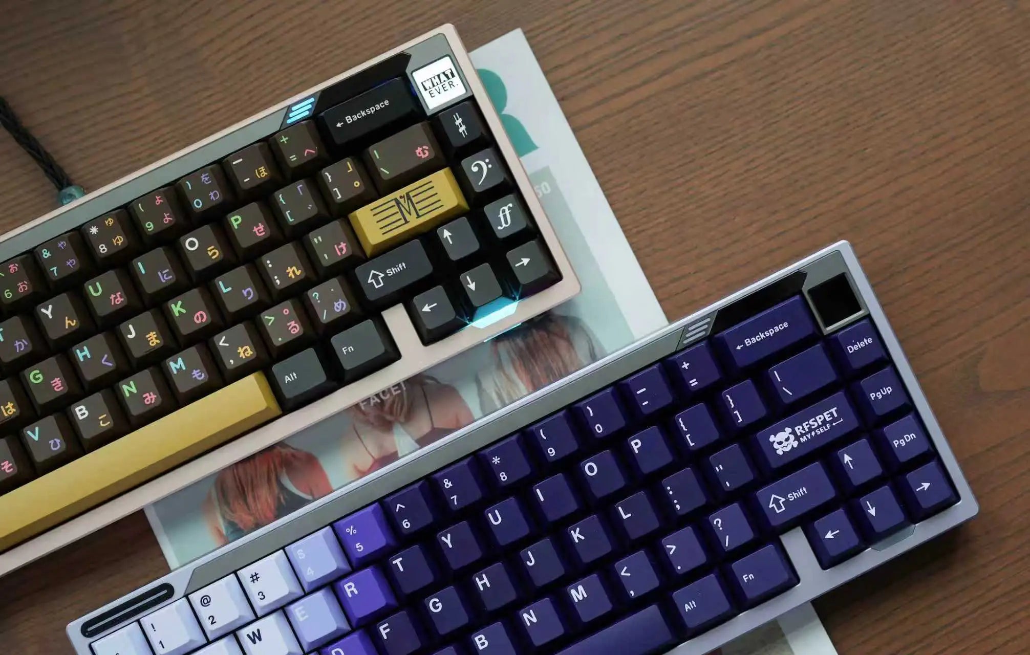 Two mechanical keyboards on a wooden surface with a magazine underneath.
